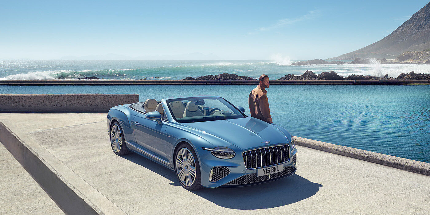 Bentley Zurich New Bentley Continental GTC Azure convertible front view in Light Windsor blue paint with 22 inch ten spoke wheels parked by the sea in the sunshine
