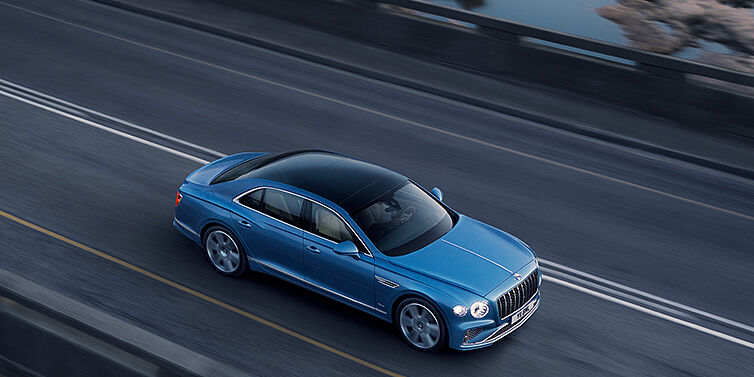 Bentley Zurich New Bentley Flying Spur Azure sedan in Light windsor blue paint by Mulliner, with 22 inch Azure wheels seen from overhead driving dynamically on a country road