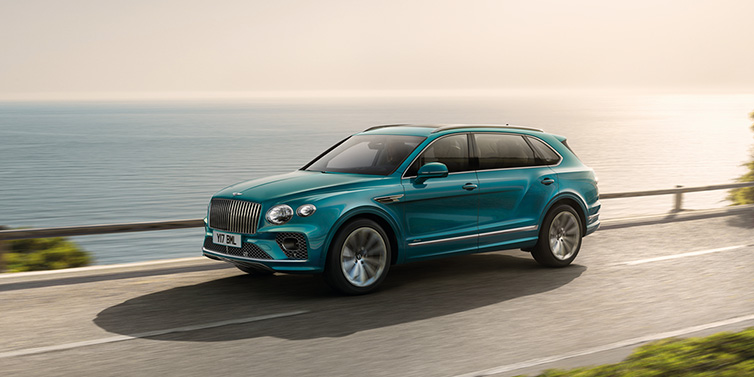 Bentley Zurich Bentley Bentayga Extended Wheelbase Azure SUV in Topaz blue paint driving dynamically by the ocean