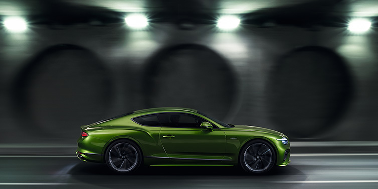 Bentley Zurich Bentley Continental GT Speed coupe profile in Tourmaline Green driving dynamically past a concrete wall at night