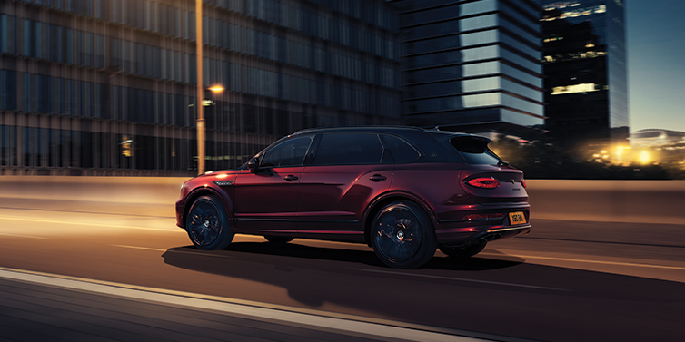 Bentley Zurich Bentley Bentayga Extended Wheelbase Mulliner SUV in Cricket Ball red paint driving dynamically in city at night