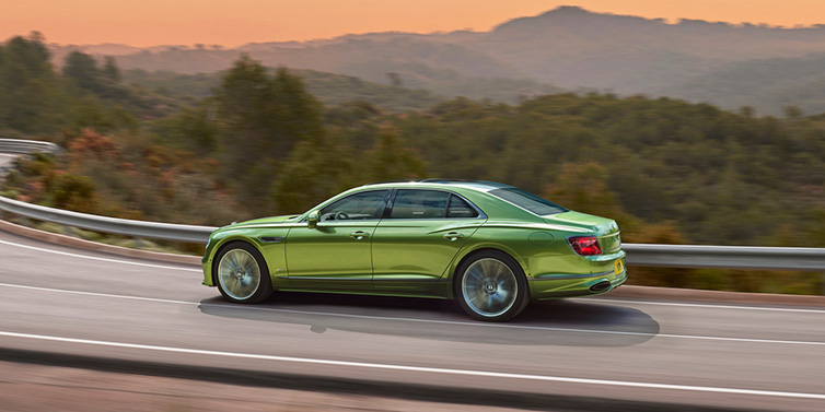 Bentley Zurich Bentley Flying Spur Speed sedan side profile in Tourmaline Green paint driving dynamically on a mountain road at sunset