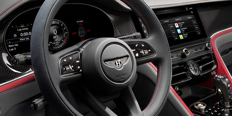 Bentley Zurich Bentley Flying Spur Speed sedan front interior detail showing steering wheel and driver screens surrounded with Hotspur red and Gravity Grey hides